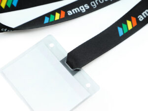 Ansicht vor dem Zusammenbau, die ein schwarzes Polyester-Lanyard mit Befestigungsschlitzen neben einem durchsichtigen Kunststoff-Ausweishalter zeigt.